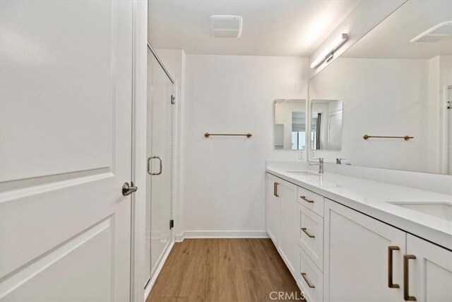 full bath featuring double vanity, a stall shower, a sink, wood finished floors, and baseboards