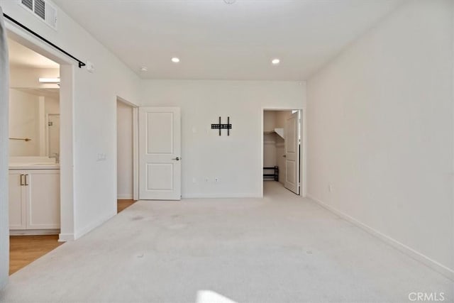 unfurnished bedroom featuring recessed lighting, a walk in closet, light colored carpet, and baseboards