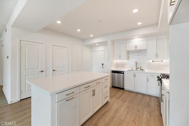 kitchen featuring stainless steel appliances, light countertops, backsplash, light wood-style floors, and white cabinetry