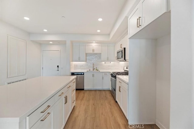 kitchen with light wood finished floors, decorative backsplash, appliances with stainless steel finishes, white cabinets, and a sink