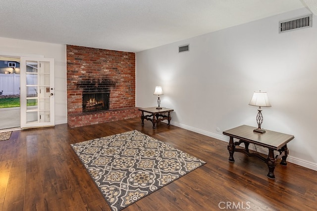 living room featuring a textured ceiling, visible vents, a fireplace, and wood finished floors