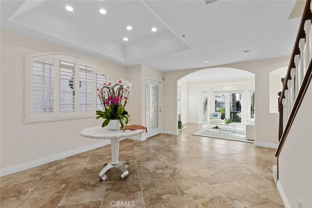 entrance foyer featuring arched walkways, recessed lighting, a raised ceiling, and baseboards