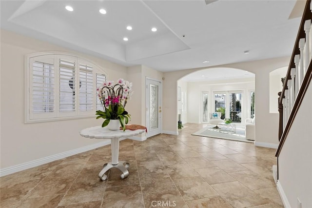 foyer featuring baseboards, recessed lighting, french doors, a raised ceiling, and arched walkways