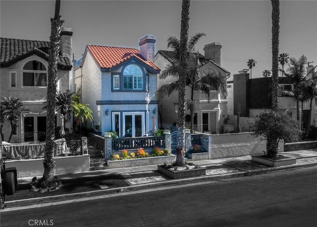 view of front of home featuring a tiled roof, stucco siding, french doors, and a chimney