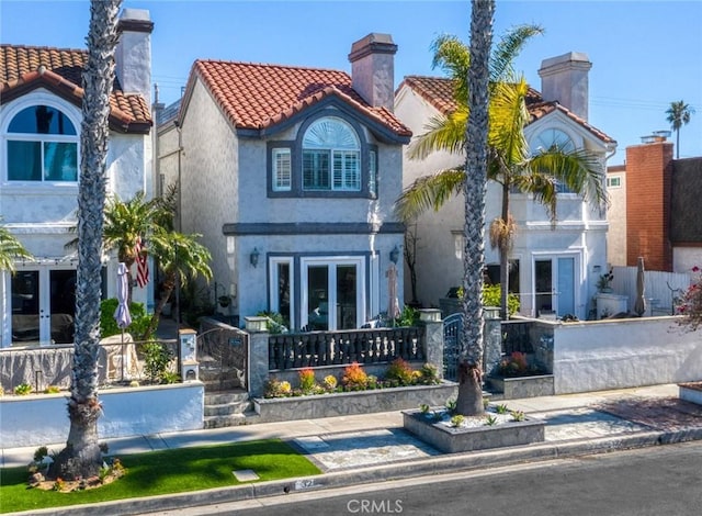 view of front of house with french doors, a tile roof, a chimney, and stucco siding