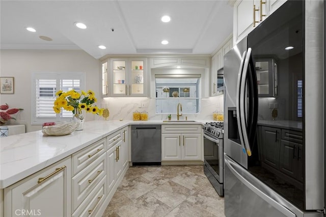 kitchen featuring a sink, backsplash, stainless steel appliances, white cabinets, and light stone countertops