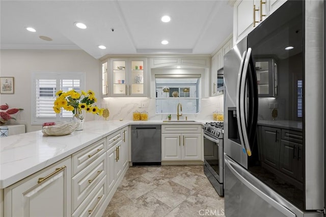 kitchen featuring white cabinets, a sink, appliances with stainless steel finishes, light stone countertops, and decorative backsplash