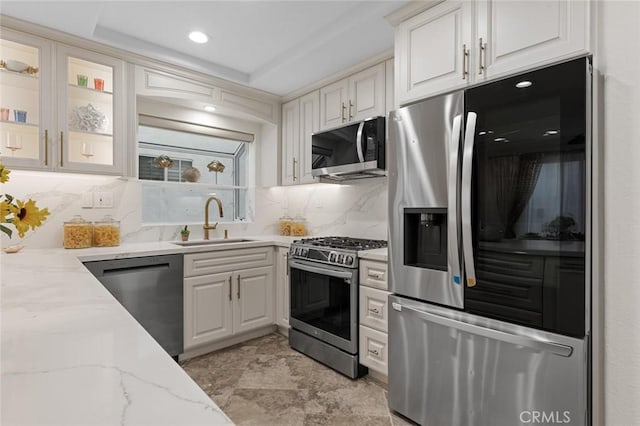 kitchen featuring backsplash, light stone counters, stainless steel appliances, white cabinetry, and a sink