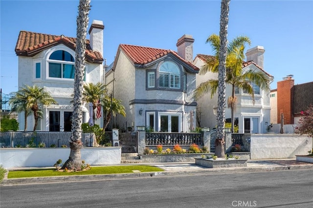 mediterranean / spanish-style house featuring a tiled roof, a fenced front yard, stucco siding, a chimney, and french doors