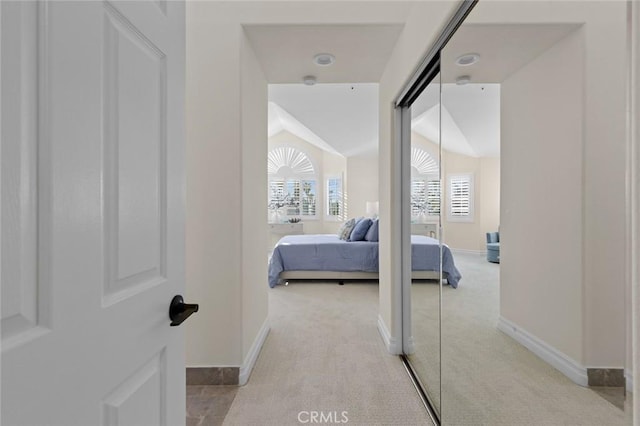 corridor with vaulted ceiling, light colored carpet, and baseboards