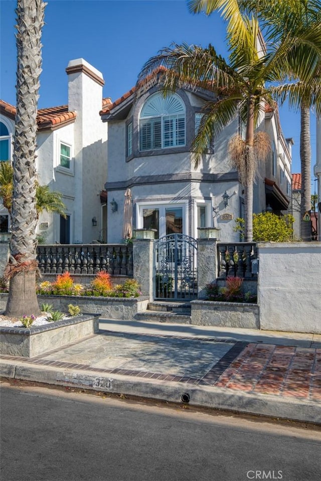 view of front of house featuring stucco siding, a tiled roof, a gate, and a fenced front yard