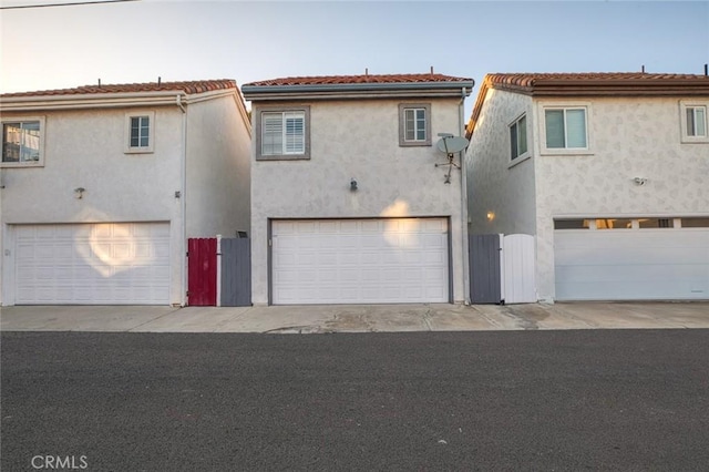 rear view of house with stucco siding, a tiled roof, an attached garage, and a gate