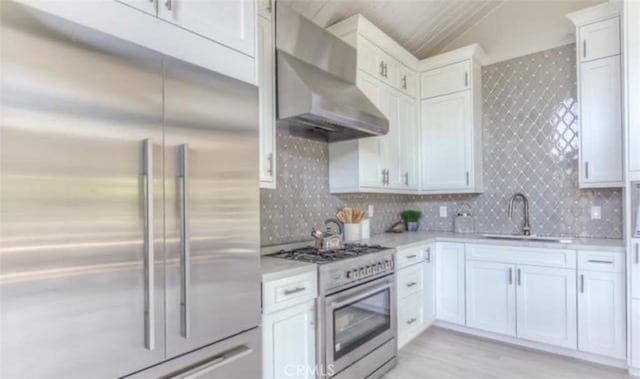 kitchen featuring premium appliances, light countertops, vaulted ceiling, a sink, and wall chimney exhaust hood