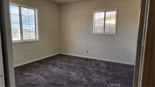 empty room featuring dark colored carpet, a wealth of natural light, and baseboards