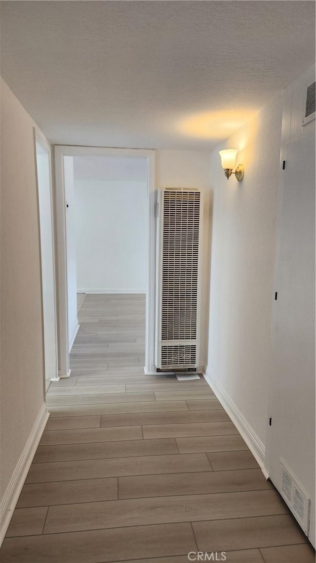 hallway with wood finish floors, a heating unit, visible vents, and a textured ceiling