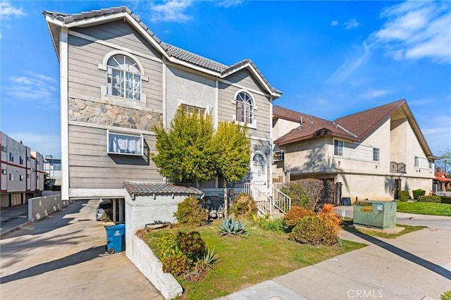 view of front of property featuring driveway, stone siding, a tile roof, and a residential view