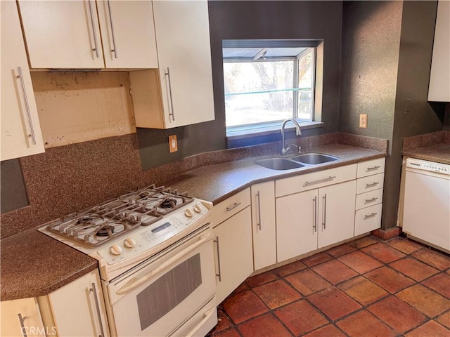 kitchen with dark countertops, white appliances, white cabinets, and a sink