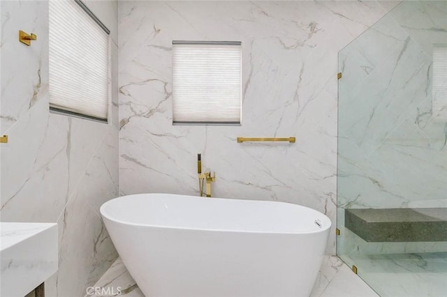 full bath with marble tiled floors, a freestanding tub, and tile walls