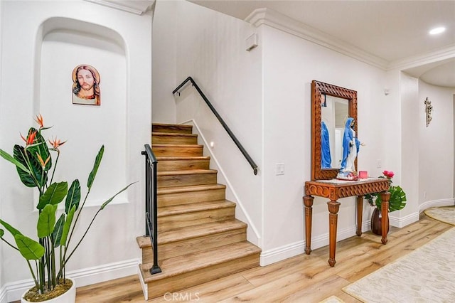 stairs with wood finished floors, ornamental molding, and baseboards