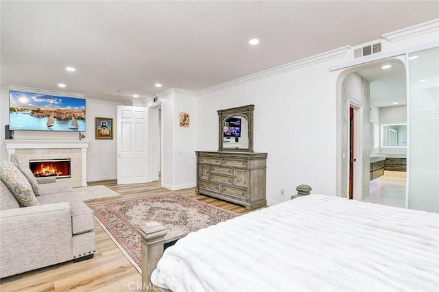 bedroom featuring ornamental molding, light wood-style flooring, a tiled fireplace, recessed lighting, and arched walkways