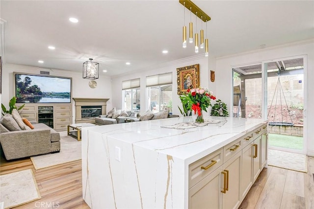 kitchen with light wood-type flooring, ornamental molding, open floor plan, light stone counters, and recessed lighting