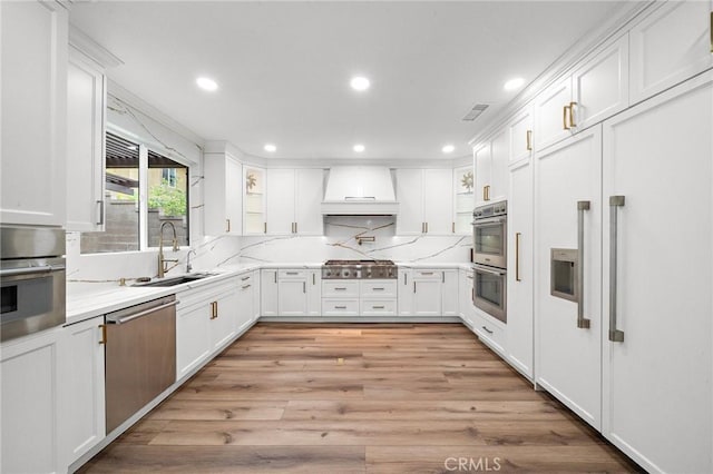 kitchen featuring a sink, premium range hood, appliances with stainless steel finishes, recessed lighting, and white cabinetry