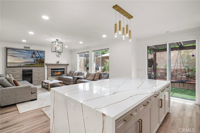 kitchen with light wood finished floors, open floor plan, a center island, recessed lighting, and a warm lit fireplace