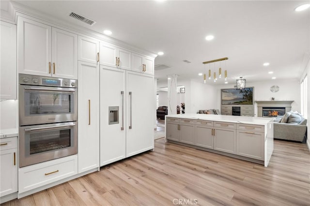 kitchen featuring double oven, a glass covered fireplace, light wood-style flooring, open floor plan, and recessed lighting
