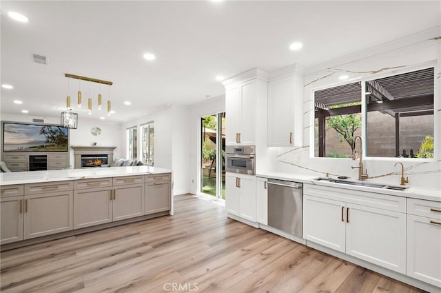 kitchen featuring stainless steel appliances, a sink, a lit fireplace, light wood finished floors, and recessed lighting