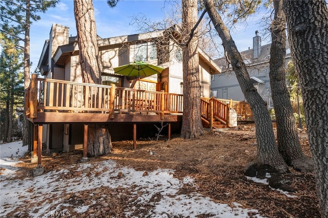 snow covered back of property with a chimney and a deck