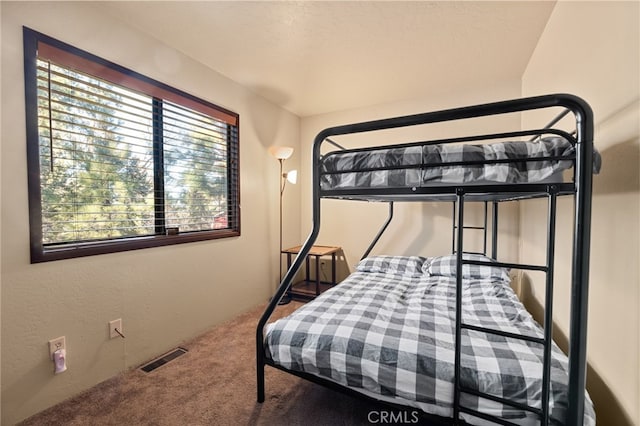 bedroom with visible vents, carpet flooring, and a textured wall