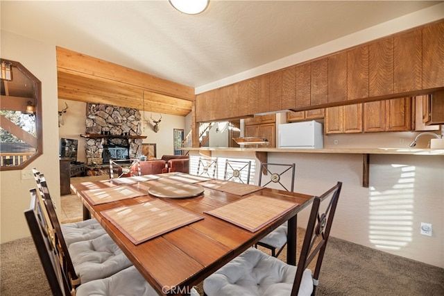 carpeted dining area featuring beamed ceiling and a stone fireplace