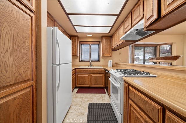 kitchen with white appliances, light tile patterned floors, brown cabinetry, light countertops, and a sink