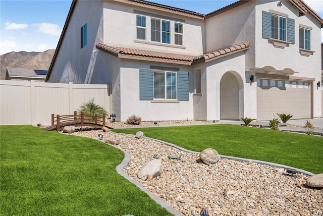 mediterranean / spanish home with an attached garage, fence, a tile roof, stucco siding, and a front lawn