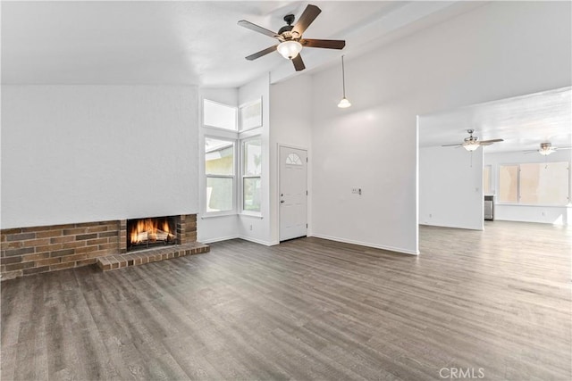 unfurnished living room with baseboards, ceiling fan, wood finished floors, a fireplace, and high vaulted ceiling