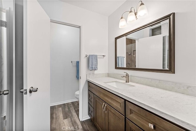 bathroom featuring baseboards, a shower, toilet, wood finished floors, and vanity