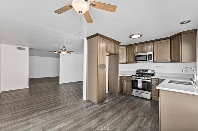 kitchen featuring a sink, open floor plan, light countertops, appliances with stainless steel finishes, and dark wood-style floors