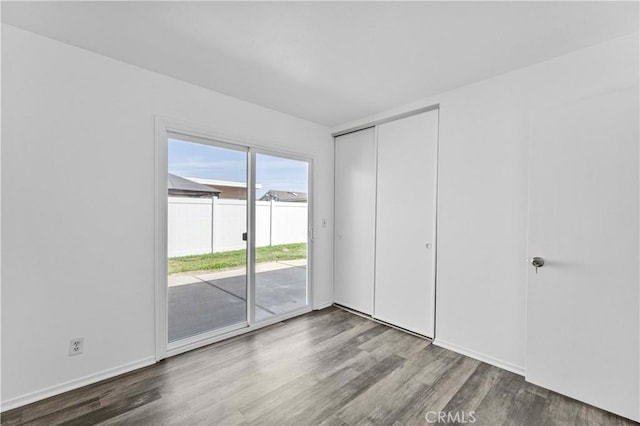 unfurnished bedroom featuring access to exterior, a closet, and wood finished floors