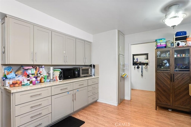 kitchen featuring black microwave, gray cabinets, light countertops, and light wood finished floors