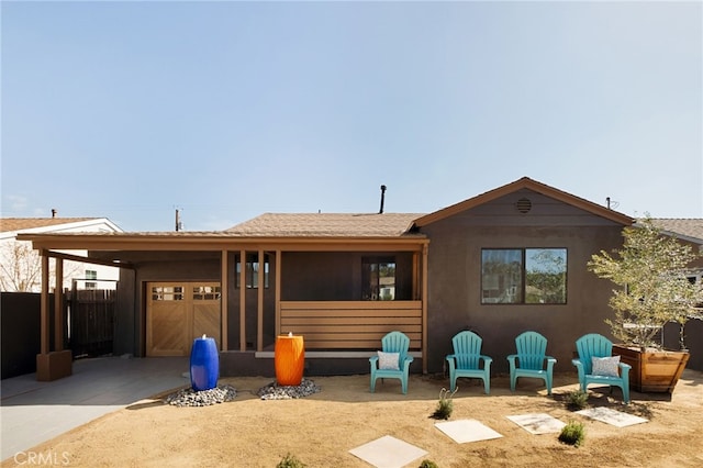 rear view of house featuring a garage, concrete driveway, fence, and stucco siding