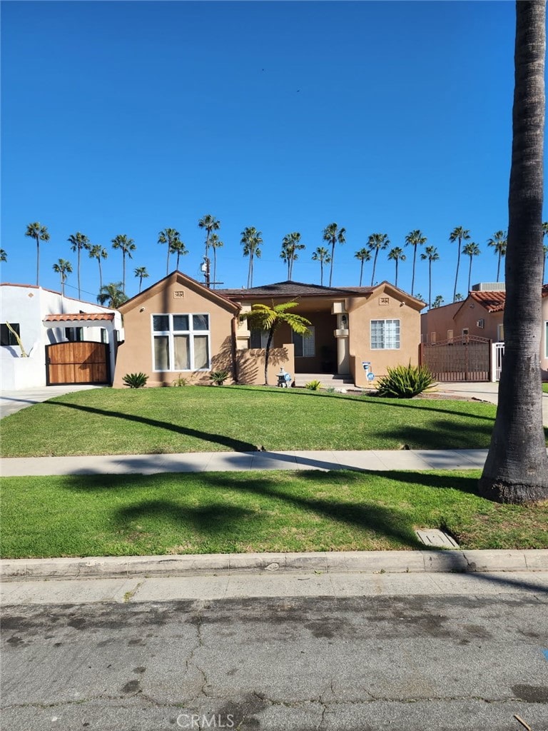 view of front facade featuring stucco siding, a front yard, and fence