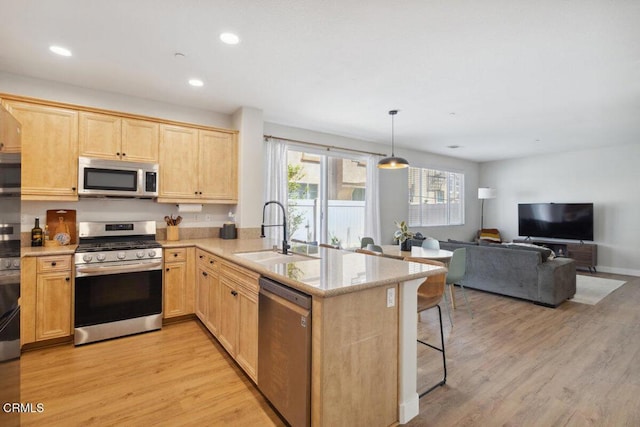 kitchen with light wood finished floors, stainless steel appliances, light brown cabinetry, a sink, and a peninsula