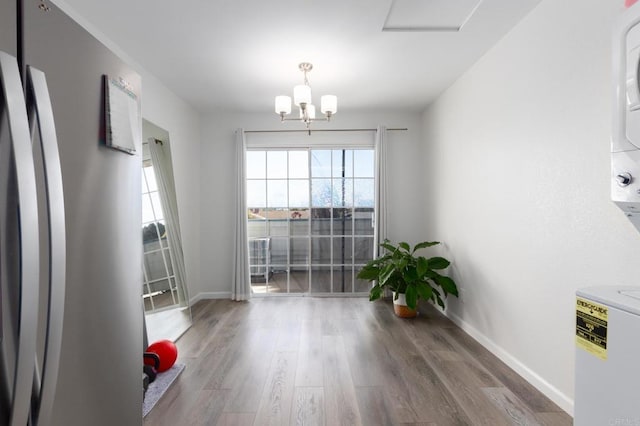 unfurnished dining area featuring an inviting chandelier, stacked washing maching and dryer, baseboards, and wood finished floors