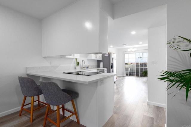 kitchen with white cabinets, a kitchen breakfast bar, a peninsula, light countertops, and light wood-type flooring