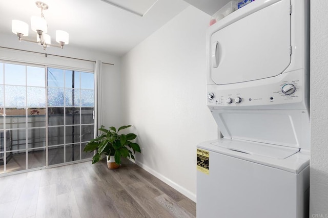 laundry area with a notable chandelier, stacked washer / drying machine, wood finished floors, laundry area, and baseboards