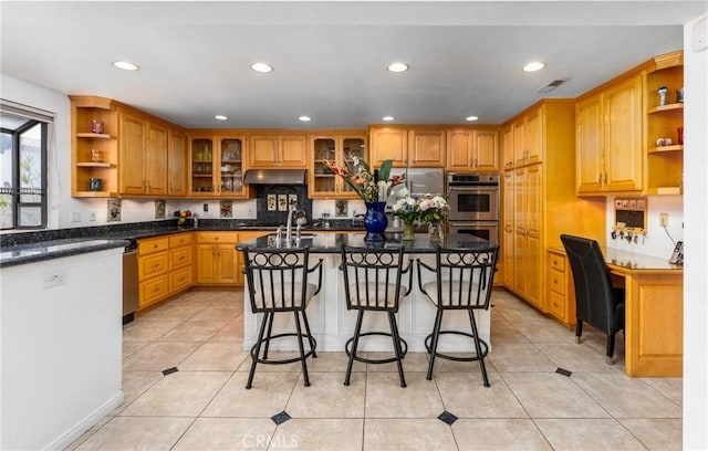 kitchen featuring double oven, under cabinet range hood, open shelves, built in desk, and a kitchen bar