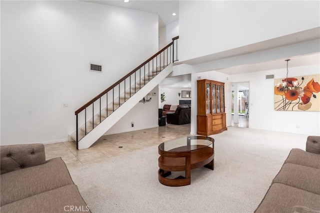 tiled living room with carpet floors, visible vents, stairway, a towering ceiling, and a chandelier