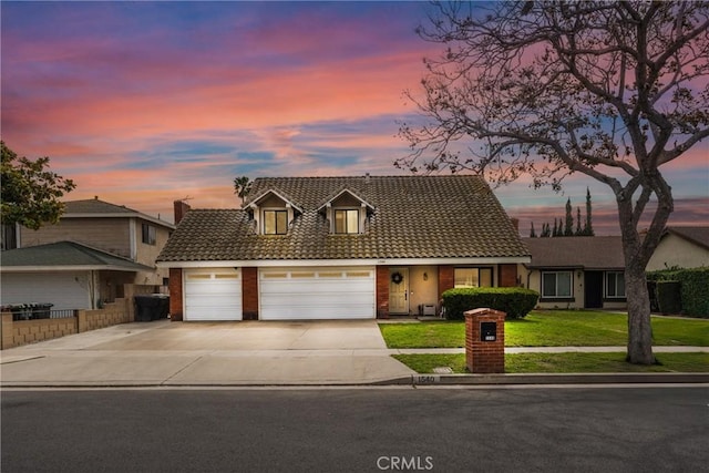 view of front of home featuring brick siding, a lawn, a garage, driveway, and a tiled roof