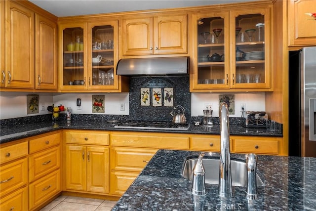 kitchen with appliances with stainless steel finishes, a sink, under cabinet range hood, and dark stone countertops