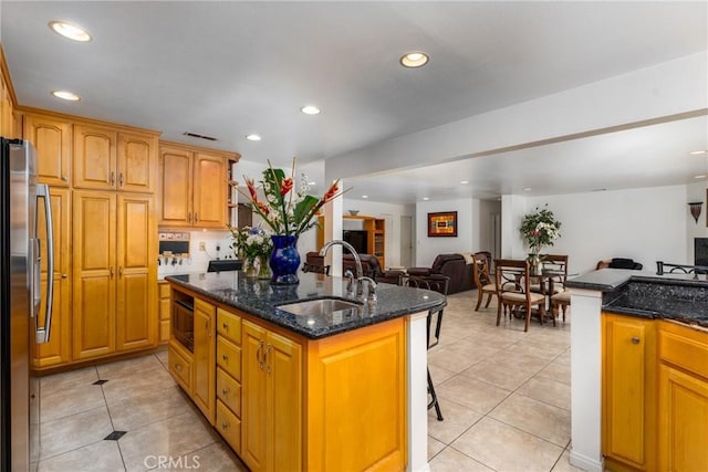 kitchen with stainless steel fridge with ice dispenser, an island with sink, open floor plan, dark stone countertops, and a sink